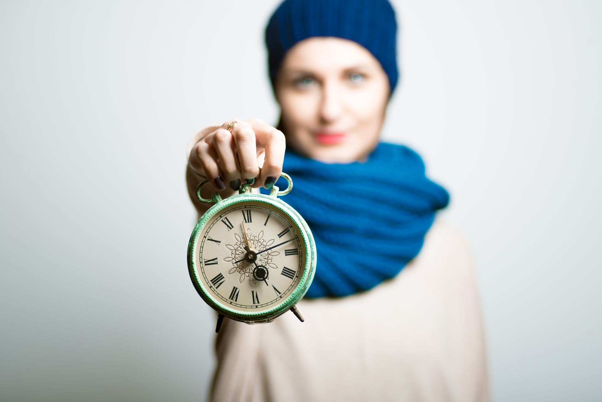 Pretty girl holds an alarm clock, dressed in winter clothes, bright lifestyle photo, isolated on a gray background